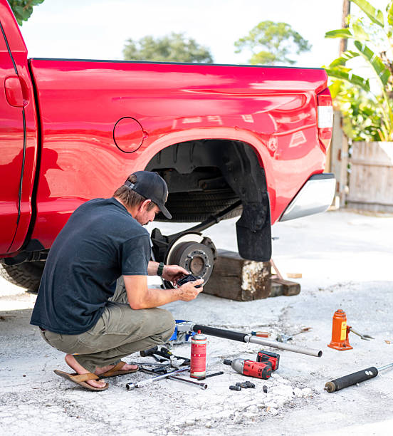 man using his phone while changing brakes in his car