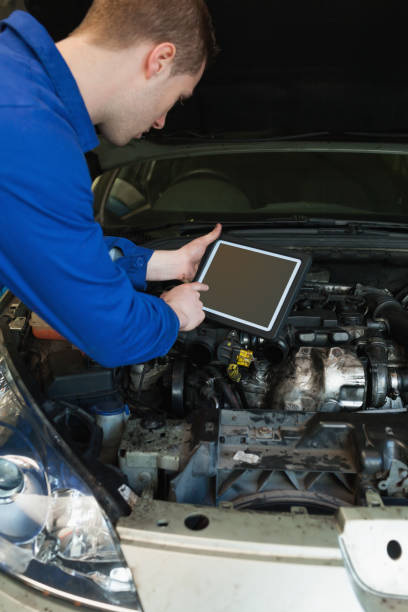 male mechanic by car with open hood using tablet computer